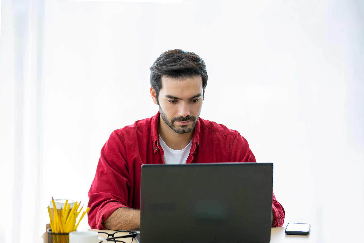 Man in red shirt using laptop.