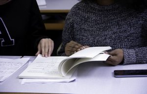 Two people flipping through a book at a table.